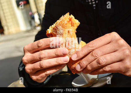 young man sitting in a table in the terrace of a cafe eating a spanish omelette sandwich Stock Photo