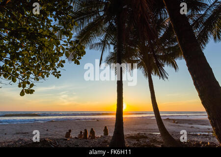 People by palm trees at sunset on Playa Hermosa beach, far south of the Nicoya Peninsula, Santa Teresa, Puntarenas, Costa Rica Stock Photo