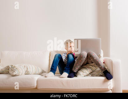 Children at home sitting on sofa, playing with laptop Stock Photo