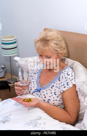 Elderly woman sitting in bed taking tablets at bedtime Stock Photo