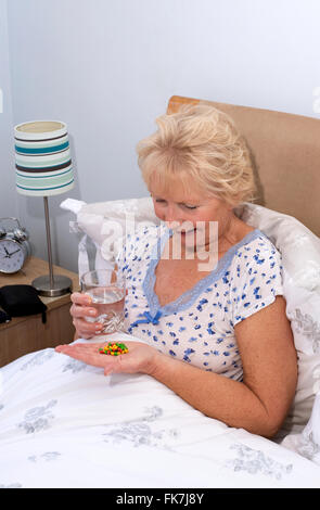Elderly woman sitting in bed taking tablets at bedtime Stock Photo