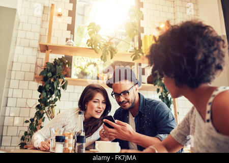 Young couple looking at smart phone while sitting in cafe with friends. Group of young people sitting at a table in restaurant a Stock Photo