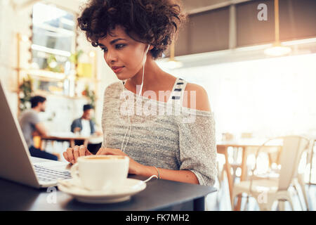 Portrait of an attractive young woman with earphones using laptop at a cafe. African american woman working on laptop computer a Stock Photo