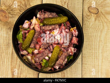 Black bowl of salad mix with beets, feta cheese, bell pepper, thin sausage and pickles on wooden background. Horizontal view fro Stock Photo