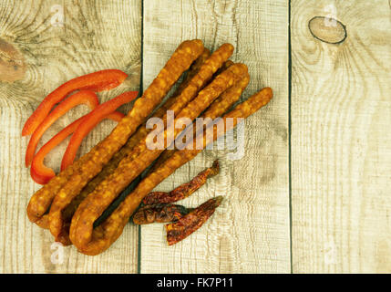 Bunch of kabanos smoked tiny sousage,fresh paprika and dried chili peppers on wooden countertop. Horizontal , from top view. Stock Photo