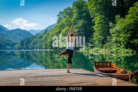 Yoga exercises at mountain forest lake. Stock Photo