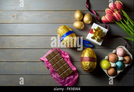 Gold easter eggs with spring tulips and gift box on a wooden table Stock Photo