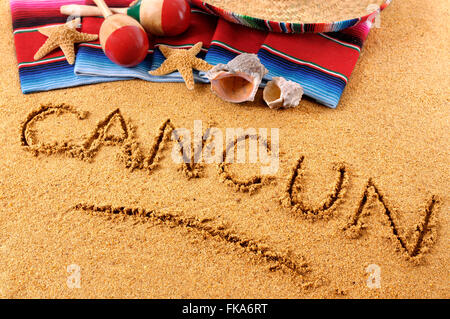 The word Cancun written in sand on a Mexican beach, with sombrero, straw hat, traditional serape blanket, starfish and maracas. Stock Photo