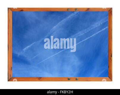 Scenic view of white vapor trails in blue sky surrounded by a wooden picture frame. Stock Photo