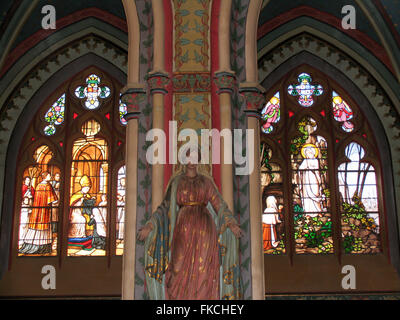 A statue of Madonna and two arched stained glass windows inside the Nevers Cathedral. Stock Photo