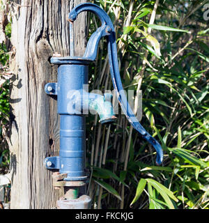 old fashioned blue cast iron water pump with handle for pumping on old worn wooden pole Stock Photo