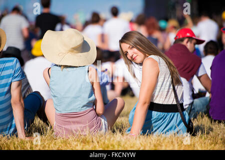 Girl with friends, teenagers, summer festival, sitting on grass Stock Photo