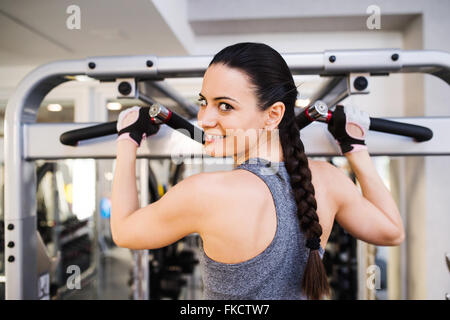 Woman in gym flexing back muscles on cable machine Stock Photo