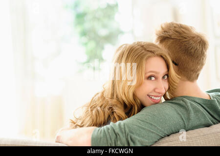 Portrait of young woman hugging boyfriend on sofa Stock Photo