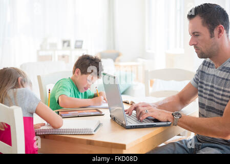 Man using laptop with two children (6-7, 8-9) writing in notepads Stock Photo