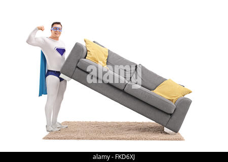 Young guy in superhero costume lifting a sofa with one hand Stock Photo