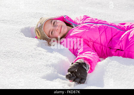 Girl (10-11) in pink jacket lying in snow Stock Photo