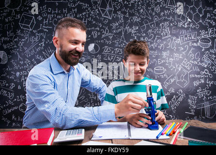 Hipster teacher with his student with microscope, big blackboard Stock Photo