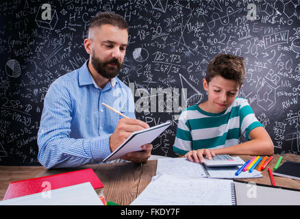 Hipster teacher with his student with calculator, big blackboard Stock Photo