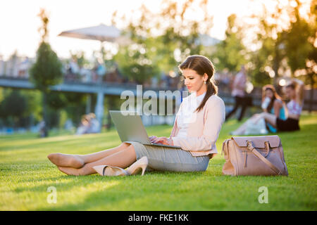 Businesswoman sitting in park working on laptop, sunny summer da Stock Photo
