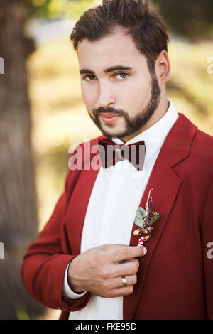 Portrait of groom in red suit with a bow tie, beard and mustache. Stock Photo