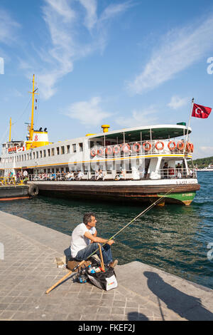 Man fishing on quayside, and passenger ferry in Karakoy Cruise Terminal, Bosphorus Strait, Istanbul, Turkey Stock Photo