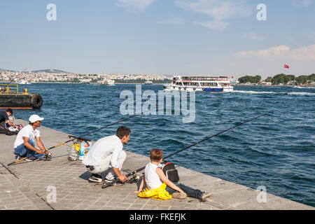 Men fishing on quayside, and passenger ferry passing, in the Bosphorus Strait, Istanbul, Turkey Stock Photo