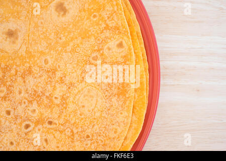 Top close view of several tomato tortilla wraps on a plate atop a wood table top. Stock Photo