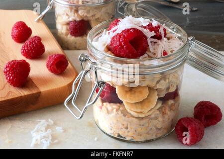 Healthy breakfast overnight oats with fresh raspberries and shredded coconut in a glass jar Stock Photo