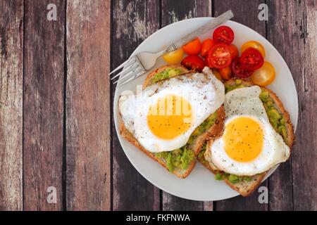 Healthy avocado, egg open sandwiches on a plate with colorful tomatoes against a rustic wood background Stock Photo