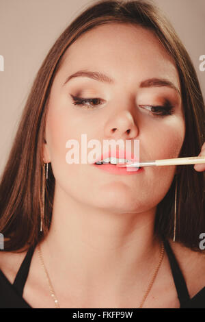 Beauty of women. Cosmetics and make up idea. Portrait of young attractive woman model aplying pink lip gloss lipstick. Stock Photo