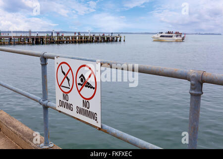 No Diving and No Swimming signs on pier railing with ocean water in the background Stock Photo