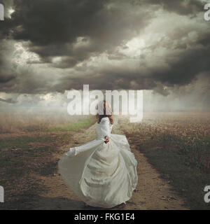 Woman dancing in desolate road. Dramatic and surreal cloudscape Stock Photo