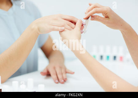 Close-up of a woman getting nail manicure by a beautician with nail file Stock Photo