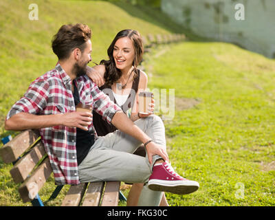 savours his coffee beautiful young couple on a park bench laughing and amused Stock Photo