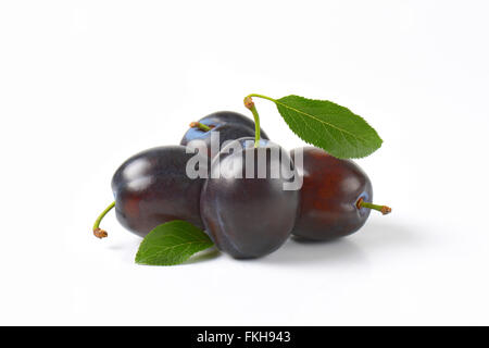 four ripe plums with leaves on white background Stock Photo