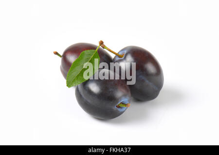 three ripe plums with leaves on white background Stock Photo