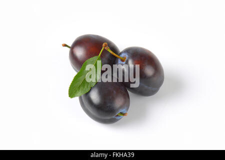 three ripe plums with leaves on white background Stock Photo