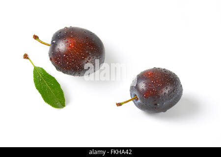 two washed plums with leaves on white background Stock Photo