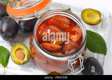 fresh and preserved plums on wooden cutting board Stock Photo