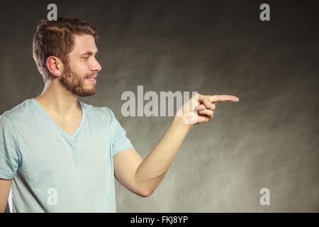 Portrait of handsome man pointing at empty blank copy space. Young guy in studio on black. Advertisement. Stock Photo