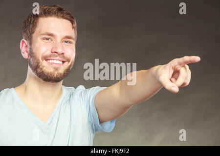 Portrait of handsome man pointing at empty blank copy space. Young guy in studio on black. Advertisement. Stock Photo