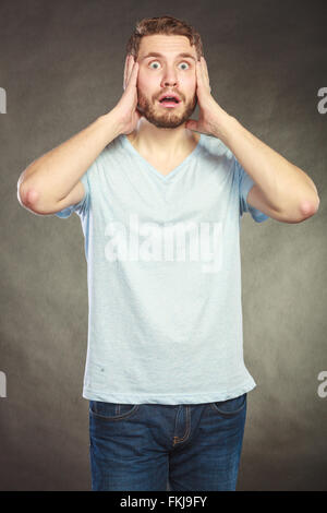 Portrait of scared afraid shocked handsome man in shirt. Young guy posing in studio on black. Stock Photo