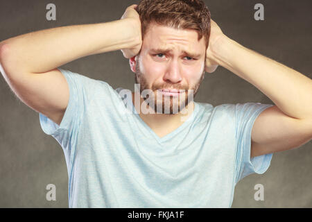 Sad miserable stressed man suffering from headache migraine pain. Young guy in studio on black. Stock Photo