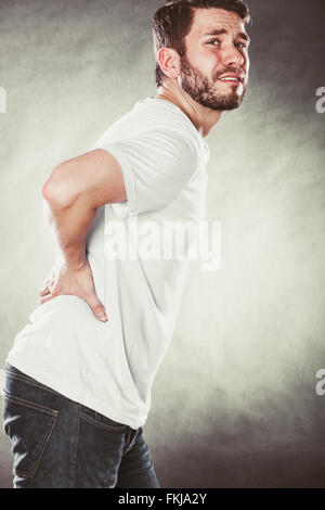 Man suffering from backache back pain. Young guy in studio on black. Stock Photo