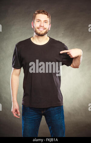 Portrait of happy handsome fashionable casual man in black blank shirt with empty copy space pointing at himself. Young guy . Stock Photo