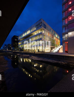 An exterior view from ground level of Orestad College in Copenhagen. The building is illuminated at night. Stock Photo