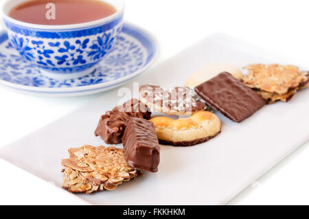 Square plate of assorted cookies near a blue decorated cup of black tea.