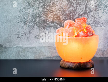 Turned on Himalayan pink salt lamp carved as a bowl on a black table. Stock Photo
