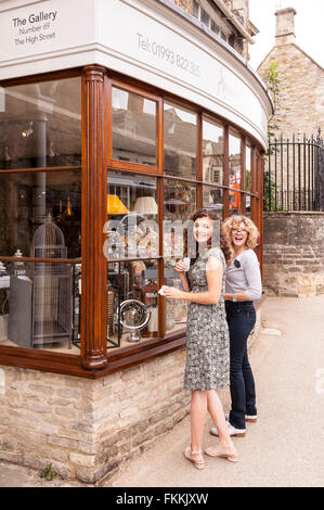 2 women clean the shop window of the Gallery shop store in Burford , Oxfordshire , England , Britain , U Stock Photo